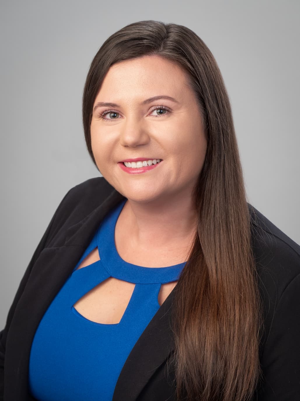 An attorney, Mirsada Kanwisher, wearing a blue dress, facing the camera, and smiling while standing outdoors holding a railing.